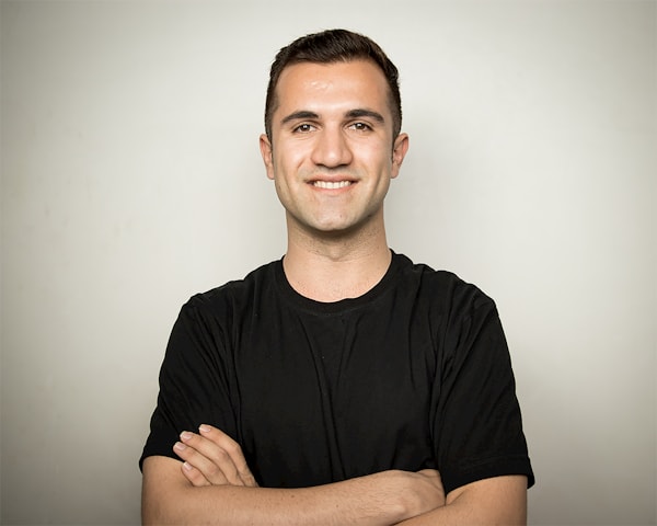 Photographe de portrait - Paris Homme souriant, les bras croisés, en tee-shirt noir sur fond clair